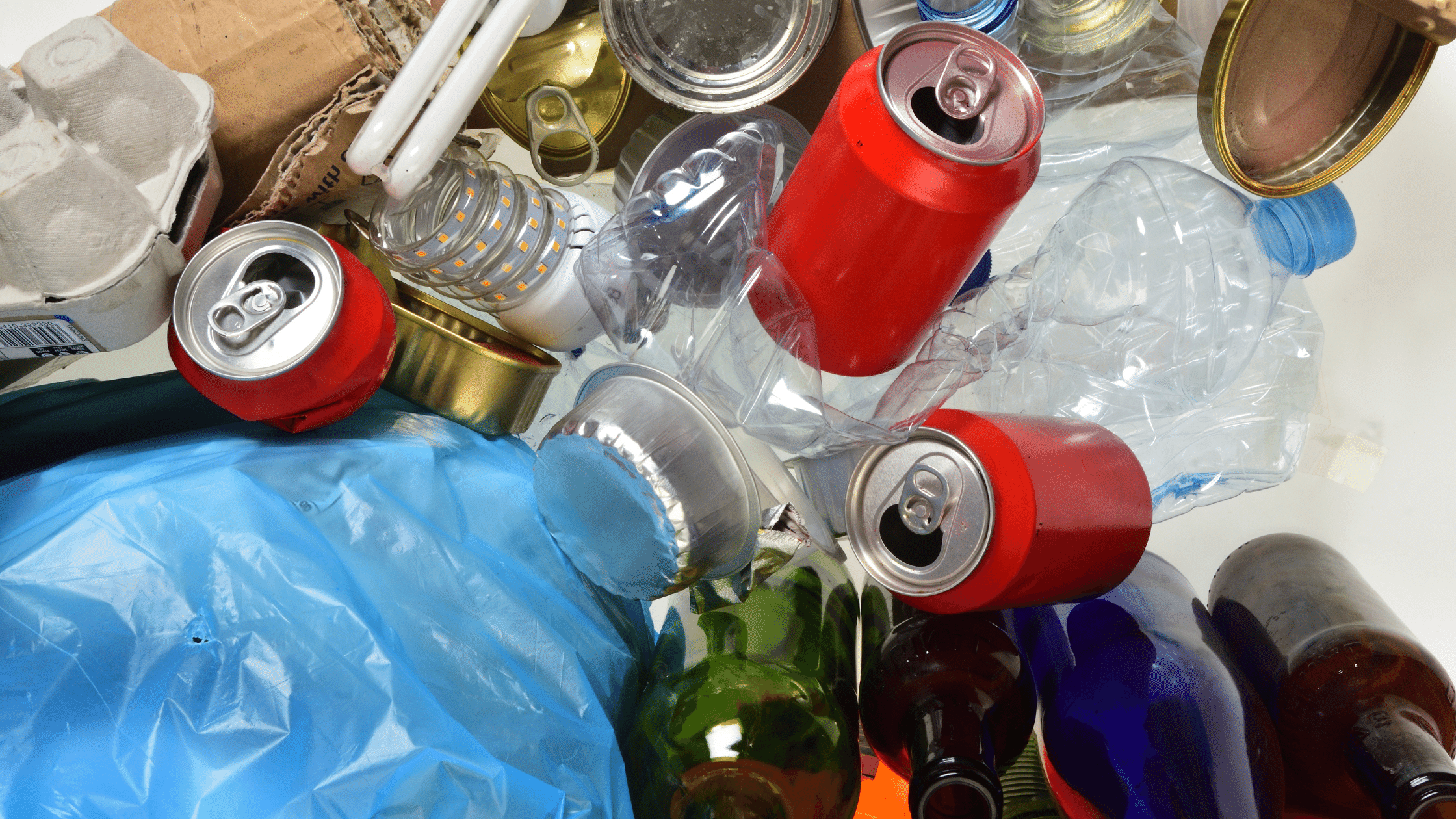 image showing pile of mixed recyclables blue plastic bag, cans, plastic bottles, lightbulb, glass bottles, etc