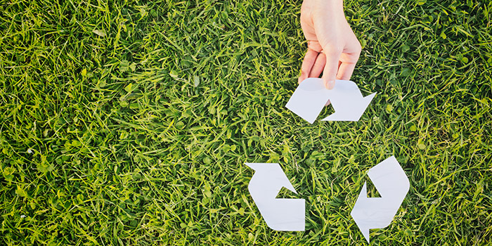 Hand making complete a recycling symbol over green grass - top view with copy space.