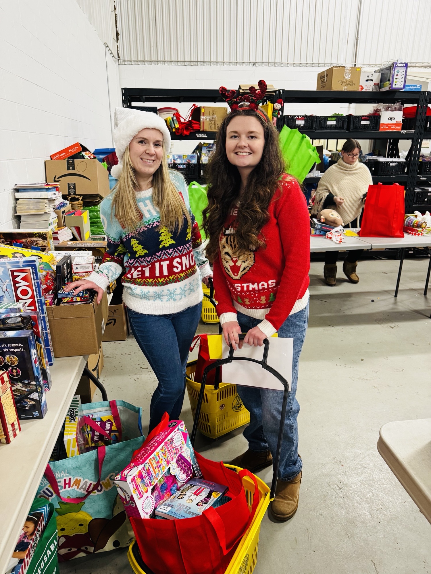 Two people wearing festive Christmas sweaters and hats organizing gift bags during a holiday donation event