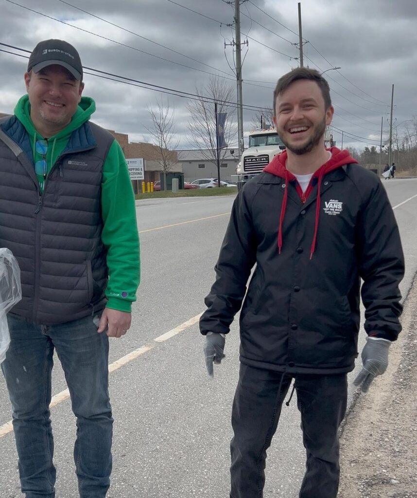 two men walking on side of road picking up trash together